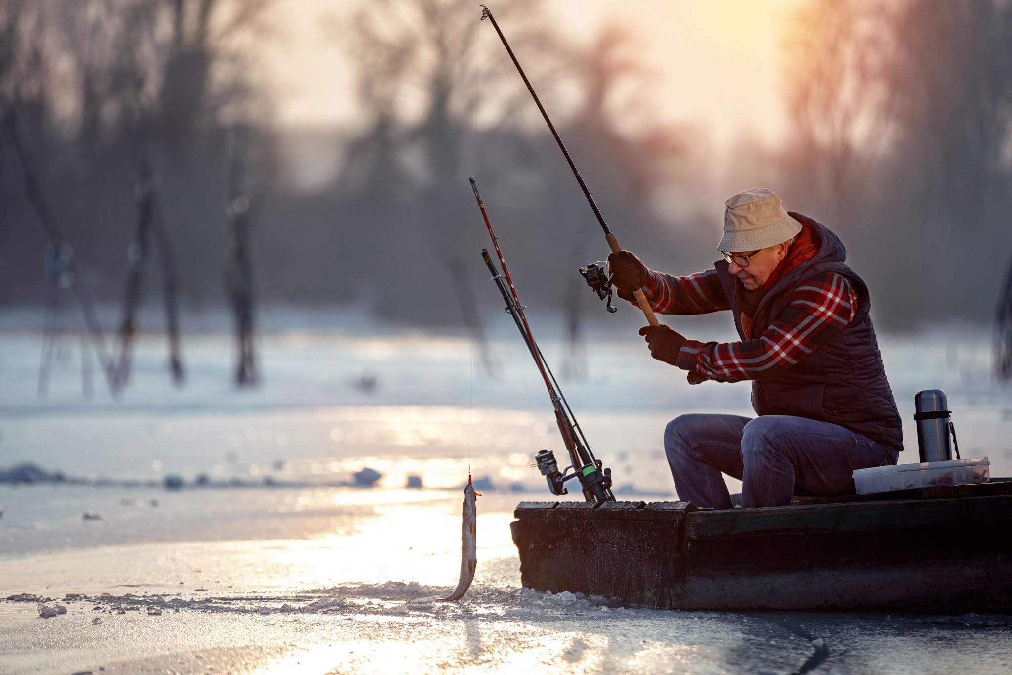 Starszy mężczyzna łowi ryby zimą w zamarzniętym jeziorze