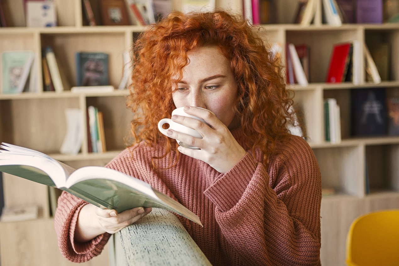 Kobieta czyta ksiązke na kanapie i pije kawe