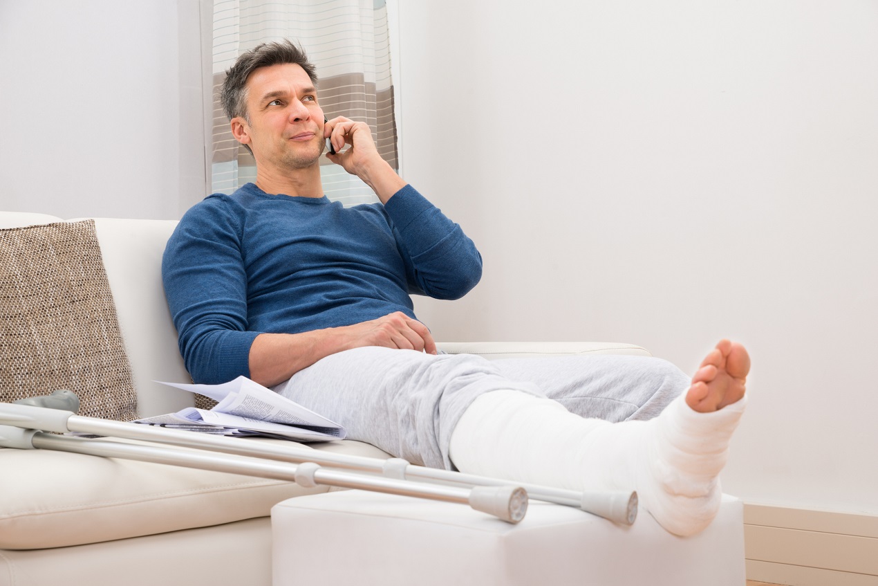 Mężczyzna ze złamana nogą rozmawia przez telefon o odszkodowaniu